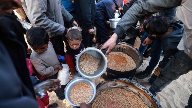 Palestinos em Rafah recebem comida antes do ifatr, refeição que representa a quebra do jejum durante o Ramadã, período sagrado para os muçulmanos