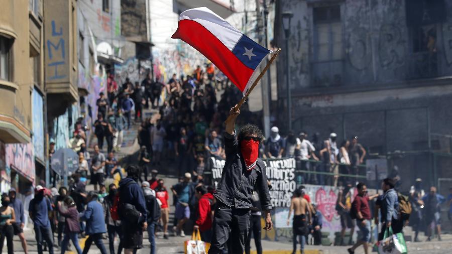 21.out.2019 - Manifestante mascarado ergue bandeira do Chile em meio aos protestos em Valparaíso, na região costeira do país - Javier Torres/AFP
