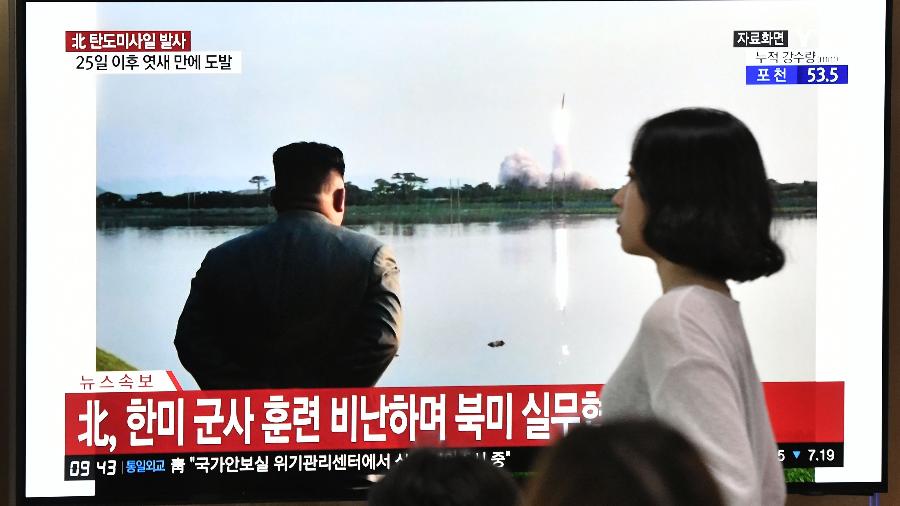 Mulher caminha em frente a uma televisão que exibe imagem do líder norte-coreano Kim Jong-un assistindo ao lançamento de um míssil - Jung Yeon-je / AFP