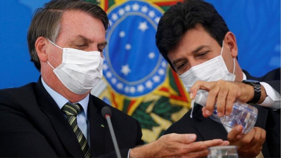 O ministro Luiz Henrique Mandetta joga álcool em gel nas mãos de Jair Bolsonaro durante entrevista coletiva. O ministro não conseguiu, até agora, desinfectar as ideias do chefe. Essa é a parte mais difícil... - Foto: Adriano Machado