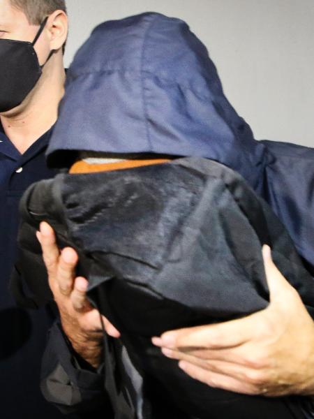 O ex-secretário estadual de Saúde do Rio de Janeiro, Edmar Santos (com o rosto coberto), é conduzido na chegada à Cidade da Polícia, na zona norte da cidade, após ser preso na manhã do dia 10 de julho - ANDRE MELO ANDRADE/MYPHOTO PRESS/ESTADÃO CONTEÚDO