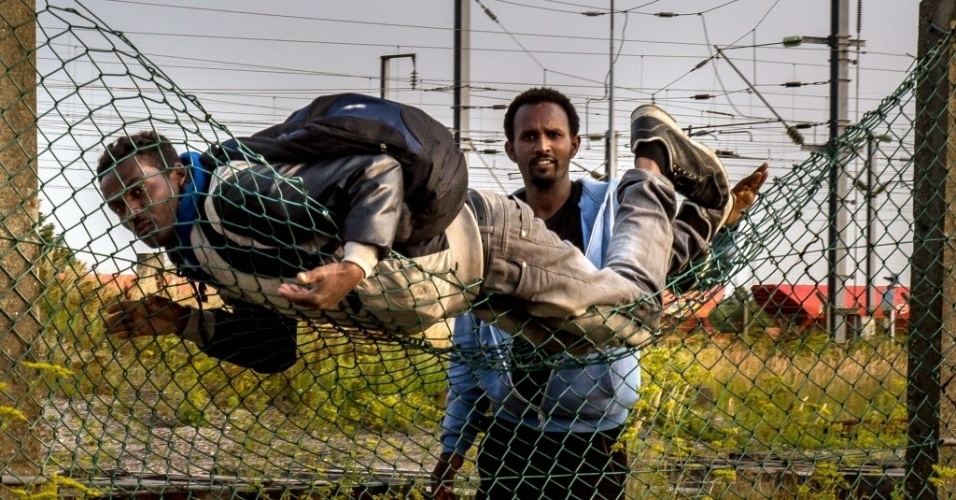 12.ago.2015 - Imigrantes pulam a cerca em Coquelles, próximo a Calais, no norte da França, para chegar à ferrovia que leva ao terminal do Eurotúnel