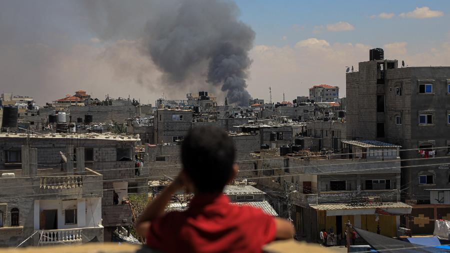 Menino observa fumaça sobre Rafah, na Faixa de Gaza, após bombardeio de Israel - 7.mai.2024-Rizek Abdeljawad/Xinhua