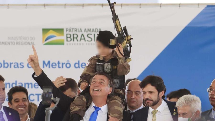 Bolsonaro coloca no ombro um menino vestido de militar e com um fuzil de brinquedo durante evento - Rodney Costa/Futura Press/Estadão Conteúdo