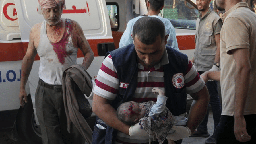 25.out.2023 - Paramédico chega ao hospital Deir Al-Balah carregando um bebê ferido em um bombardeio à faixa de Gaza