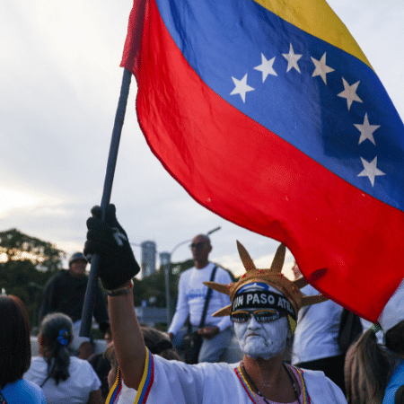 22.out.26 - Vestido como a Estátua da Liberdade, apoiador da oposição ergue bandeira da Venezuela durante manifestação que exige eleições em 2027, em Caracas, na Venezuela 22.out.26 - Vestido como a Estátua da Liberdade, apoiador da oposição ergue bandeira da Venezuela durante manifestação que exige eleições em 2027, em Caracas, na Venezuela