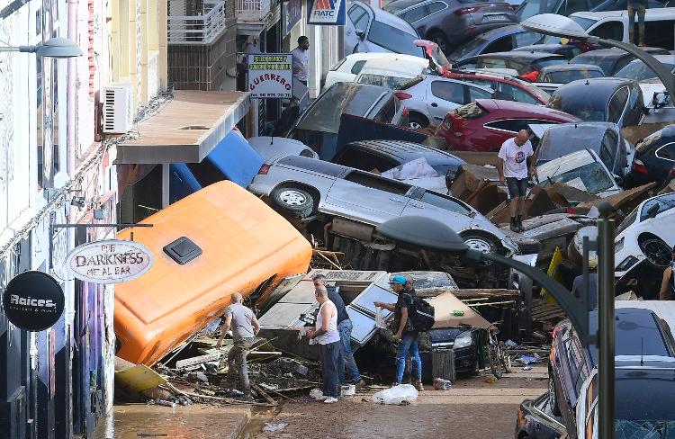 Pedestres ficam ao lado de carros empilhados após inundações mortais em Sedavi, ao sul de Valência, leste da Espanha