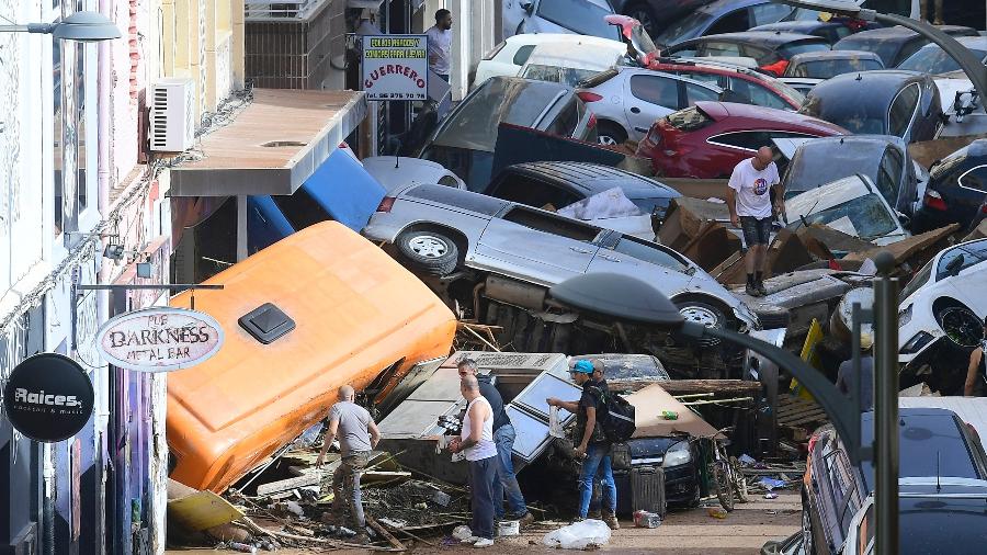 Pedestres ficam ao lado de carros empilhados após inundações mortais em Sedavi, ao sul de Valência, leste da Espanha