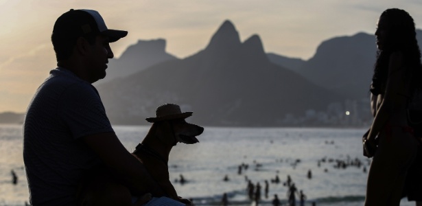 27.dez.2016 - Com um cachorro "vestindo" um chapéu personalizado no colo, homem observa a praia de Ipanema, na zona sul do Rio de Janeiro, pouco após o pôr do sol - Marco Antônio Teixeira/UOL