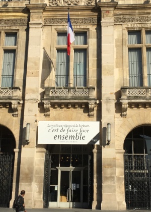 Homem olha para sede da prefeitura de Saint-Denis, no norte de Paris, com cartaz que diz: "A melhor resposta à barbárie é lidarmos juntos" - Carolina Vila-Nova/UOL