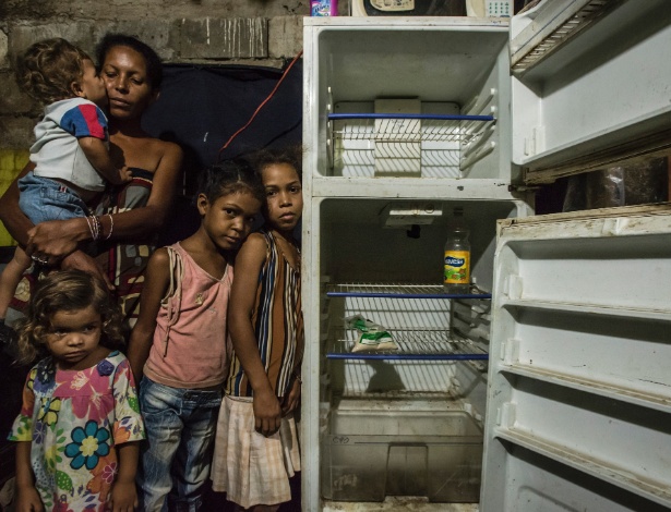 Leidy Cordova, 37, com quatro de seus cinco filhos, mostra a única comida que tem em casa: um saco de farinha e um frasco de vinagre na geladeira quebrada, em Cumaná, na Venezuela - Meridith Kohut/The New York Times