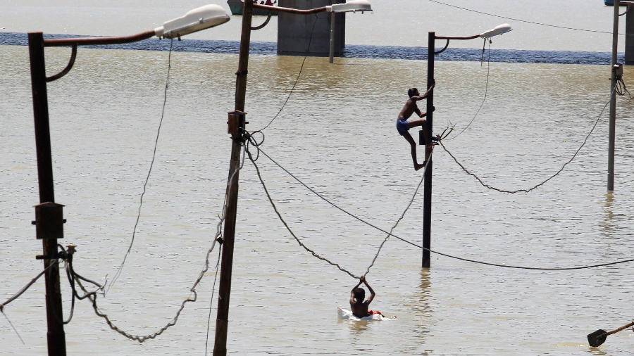 21.ago.2016 - Meninos escalam postes para fugir de enchente do rio Ganga, em Allahabad, na Índia - Jitendra Prakash/Reuters