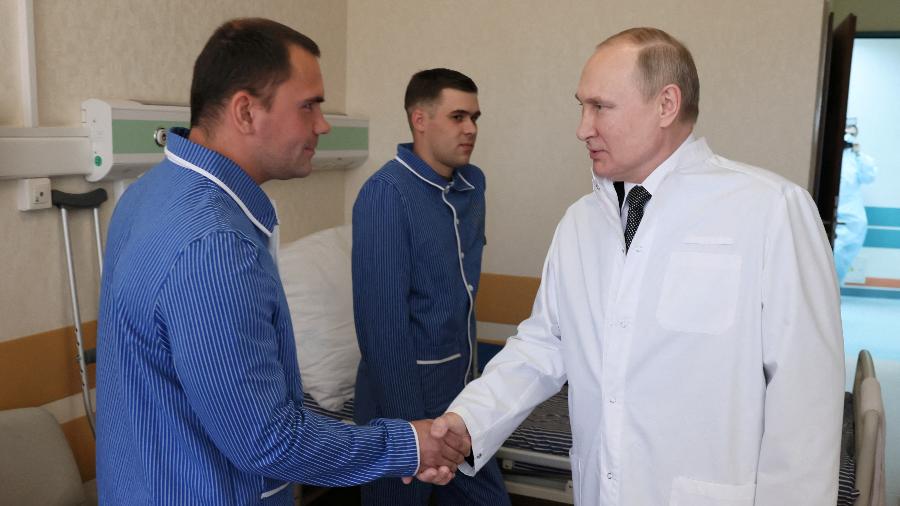 Vestindo um jaleco branco e acompanhado pelo ministro da Defesa, Sergey Shoigu, o líder russo conversou e cumprimentou os combatentes - SPUTNIK/via REUTERS