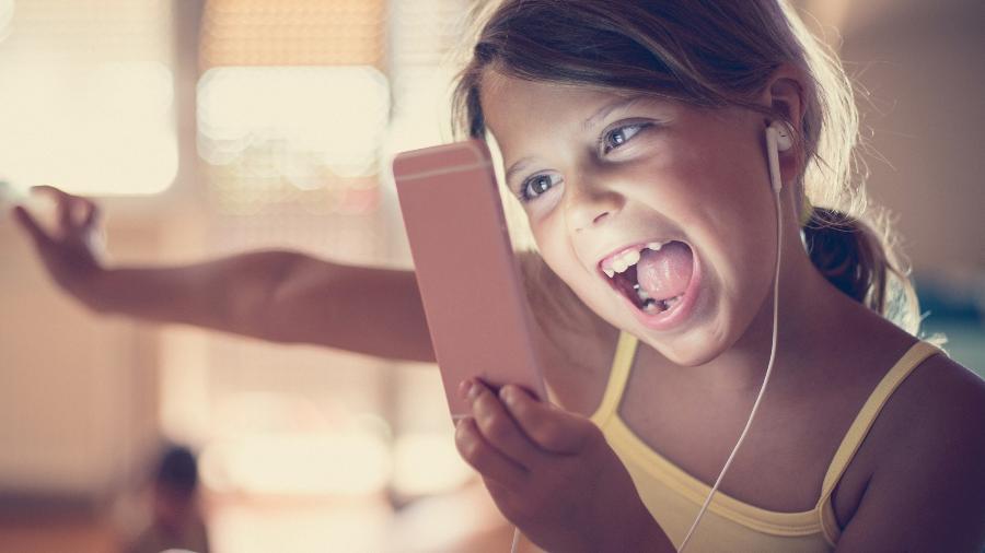 Menina usa celular e fones de ouvido; criança; redes sociais; música para crianças; streaming de música; ouvir música no celular - Mladen Zivkovic/iStock