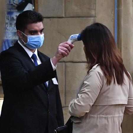 22.jan.2020 - Funcionário de cassino em Macau mede temperatura de uma mulher antes de sua entrada no prédio - Anthony Wallace/AFP