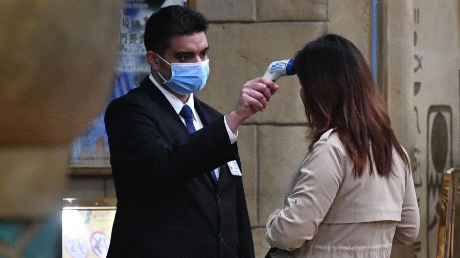 22.jan.2020 - Funcionário de cassino em Macau mede temperatura de uma mulher antes de sua entrada no prédio - Anthony Wallace/AFP
