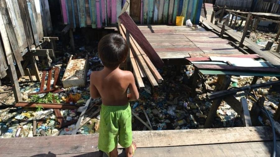 Criança entre casas de palafita em curso de água cheio de lixo - Marcello Casal/Agência Brasil