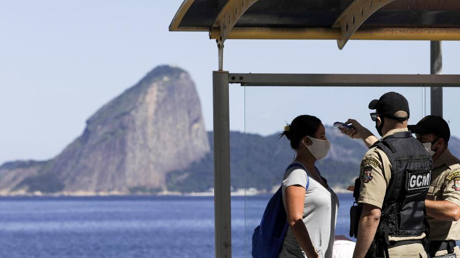 Guardas municipais verificam temperatura de mulher em ponto de ônibus no Rio de Janeiro - RICARDO MORAES