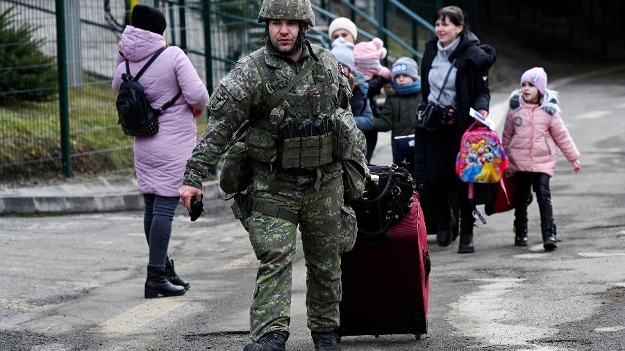 Soldado ajuda a carregar bagagem de refugiados da Ucrânia que atravessam a fronteira com a Eslováquia - Radovan Stoklasa/Reuters