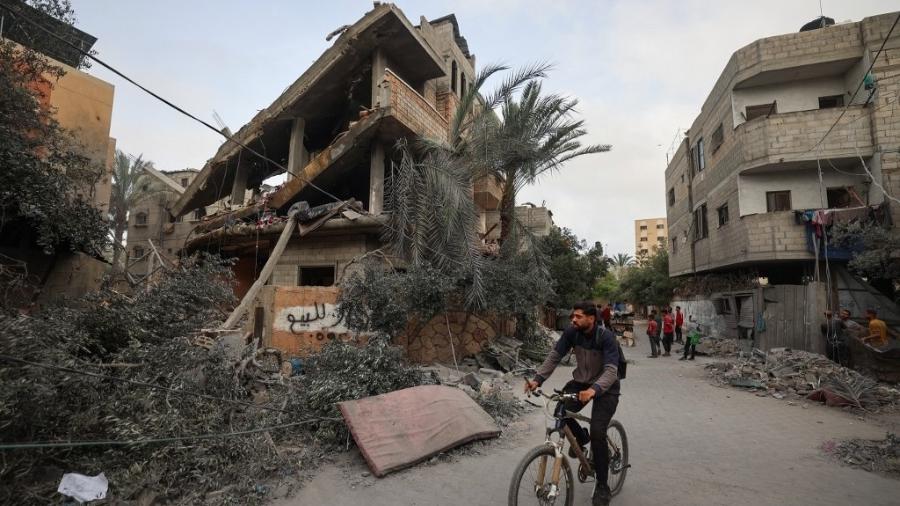 Um palestino pedala em frente a uma casa atingida por ataques israelenses no campo de refugiados de Nuseirat, no centro da Faixa de Gaza, em 18 de maio de 2025 Um palestino pedala em frente a uma casa atingida por ataques israelenses no campo de refugiados de Nuseirat, no centro da Faixa de Gaza, em 18 de maio de 2025
