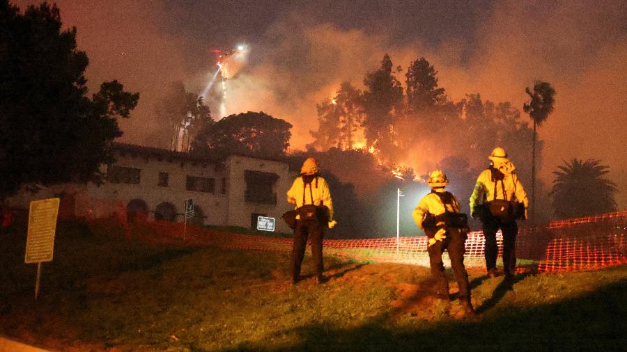 08.jan.25 - Um helicóptero realiza um lançamento de água, enquanto fumaça e chamas sobem do incêndio Sunset nas colinas com vista para o bairro de Hollywood em Los Angeles, Califórnia, EUA