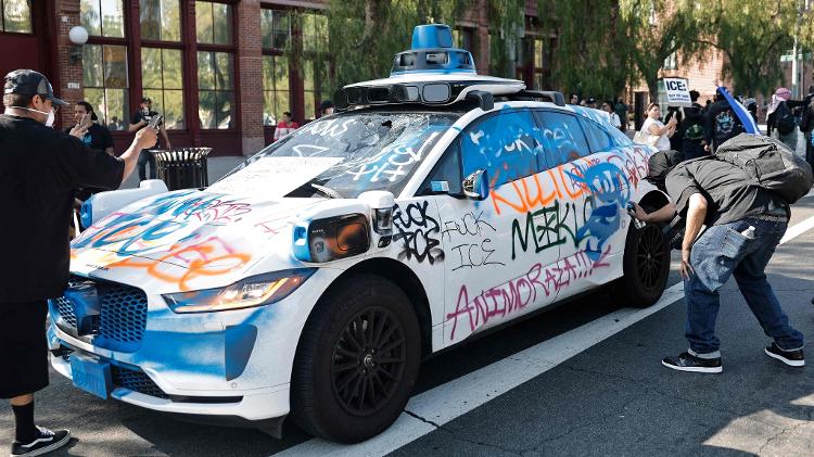 Manifestante picha lateral de carro autônomo da Waymo, durante protestos contra a perseguição a imigrantes em Los Angeles, nos EUA