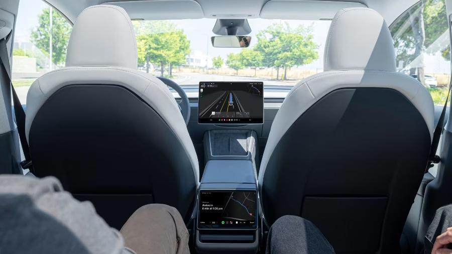 Visão do banco traseiro do Model Y, da Tesla, usado como Robotaxi; há uma tela na parte traseira do carro para poder acionar a corrida