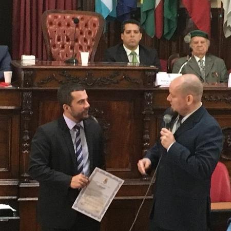 Carlos Jordy, sob o olhar de Flávio Bolsonaro, entrega homenagem a integralista Breno Zarranz - Reprodução de WhatsApp