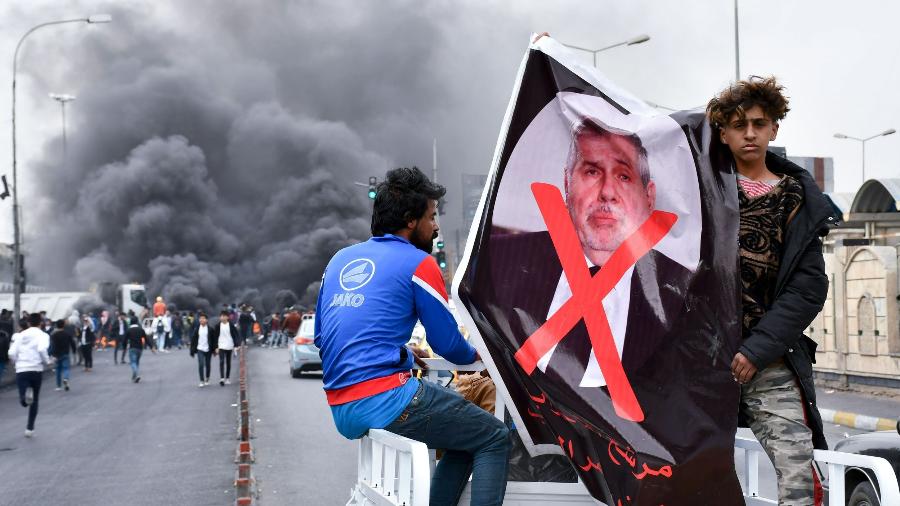 Manifestantes iraquianos levantam uma foto do premiê Mihammed Allawi em protesto contra o governo em Nasiriyah, no Iraque - Asaad Niazi/AFP
