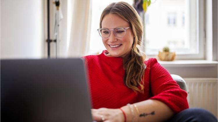 White woman in red blouse works in front of computer - Getty Images - Getty Images