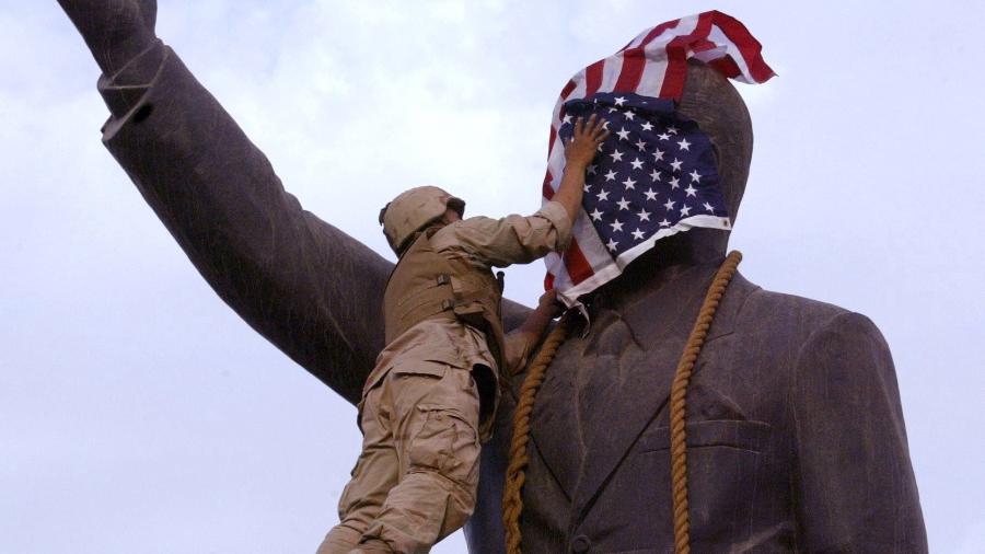 Ataque dos EUA ao Iraque: o marine Edward Chin cobre o rosto de estátua de Saddam Hussein com bandeira americana, que foi retirada depois de vaias dos iraquianos, em Bagdá, após a tomada da capital por soldados da coalizão. A US Marine covers the face of Iraqi President Saddam Hussein"s statue with the US flag in Baghdad"s al-Fardous square 09 April 2003. The flag was removed shrtly afterwards and replaced by the old Iraqi flag. US troops moved into the heart of the Iraqi capital meeting little resistance. AFP PHOTO/Ramzi HAIDAR - Ramzi HAIDAR-9.abr.2003/AFP