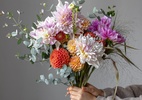 As flores dos buquês do verão 2025 - A woman holds in her hand a festive flower arrangement with bright chrysanthemum flowers, a festive bouquet.