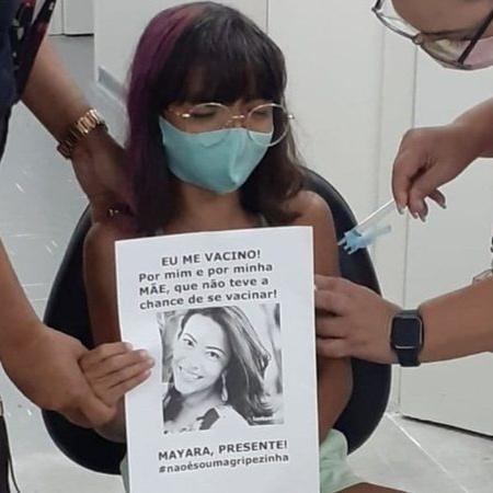 Menina segura cartaz com foto da mãe no momento da vacinação - Divulgação / TV Globo