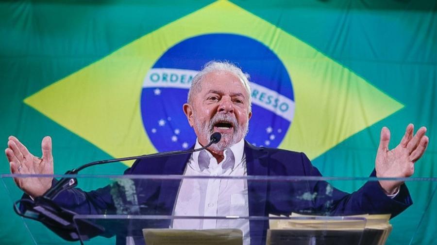 Lula fala em microfone e bandeira do Brasil aparece ao fundo - Divulgação
