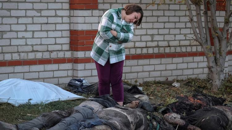 Uma residente local observa corpos no local de um ataque militar russo, enquanto especialistas policiais trabalham na vila de Hroza, na região de Kharkiv, Ucrânia, em 5 de outubro de 2023.