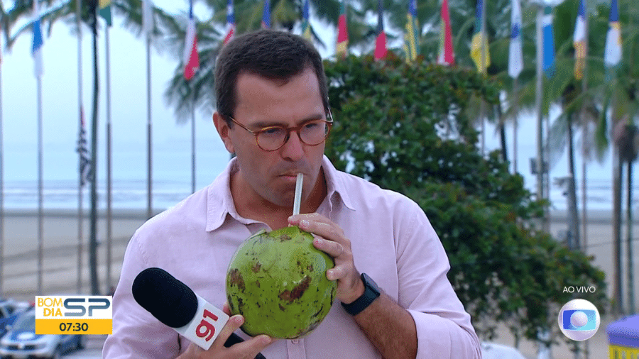 Rodrigo Bocardi tomando água de coco na praia ao vivo durante a exibição do Bom Dia SP - Reprodução/TV Globo