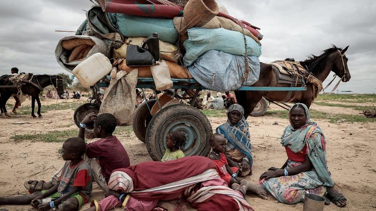 Uma família sudanesa que fugiu do conflito em Murnei, na região sudanesa de Darfur, senta-se ao lado de seus pertences enquanto espera ser registrada pelo ACNUR ao cruzar a fronteira entre o Sudão e o Chade em Adre, Chade, 26 de julho de 2023. 