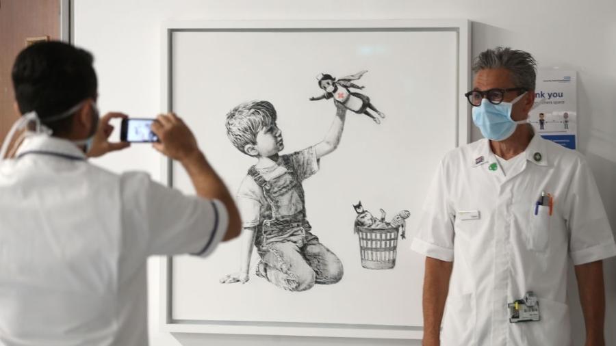 Profissional da saúde posando ao lado da obra de Banksy chamada "Game Changer" - PA Images via Getty Images