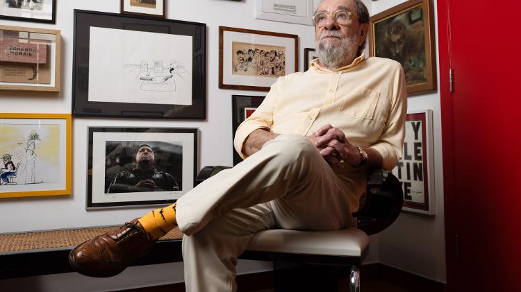 Fernando Morais usa meias de morcegos durante entrevista em São Paulo; na parede, foto de Chávez