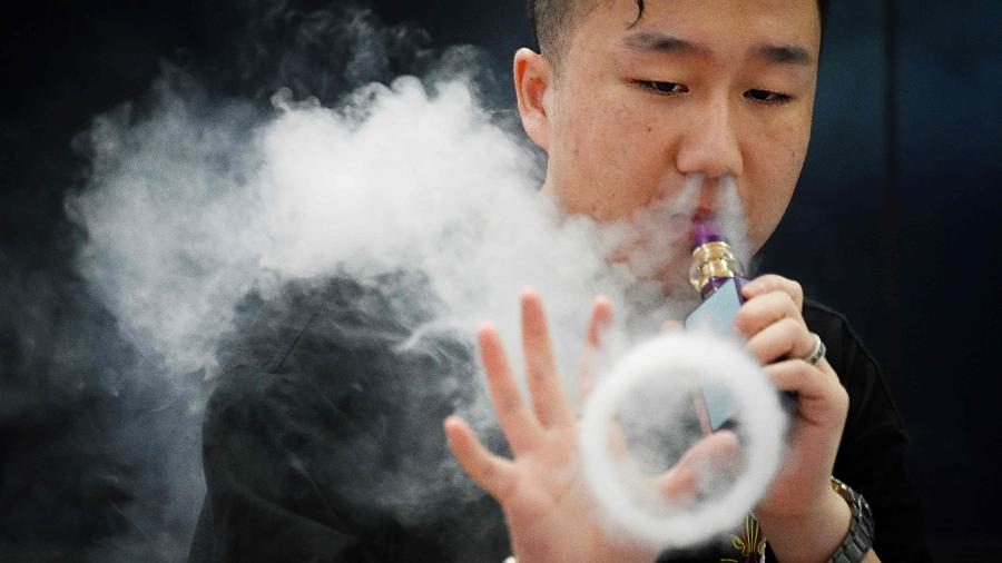 Promotor faz figuras com o vapor de e-cigarro em exposição em Pequim (China) - AFP