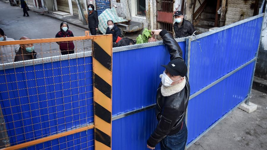 Entregador passa alimentos por cima de barreira em bairro de quarentena em Wuhan, epicentro do surto de coronavírus na China - AFP