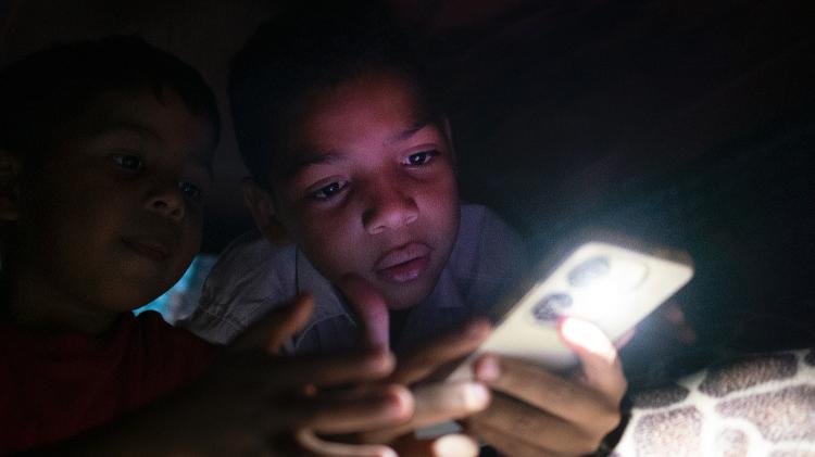 Crianças brincam no celular com a casa às escuras no bairro de Petare, em Caracas