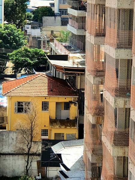 Imagem de sobrado na rua Alves Guimarães, em Pinheiros, que tem parte de sua estrutura embaixo de andaimes da construção do prédio ao lado