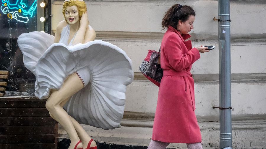 Mulher passa olhando para smartphone e mal percebe estátua de Marilyn Monroe - AFP