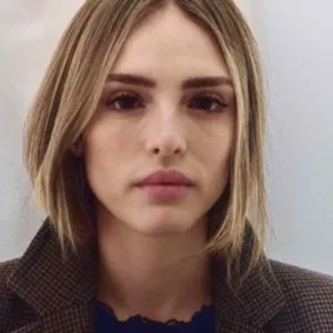 Isabelle Drummond com cabelo loiro e curto e blusa de frio com fundo branco