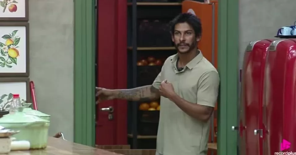 Shia Phoenix de roupa bege, falando e gesticulando, sério, sem olhar para a câmera