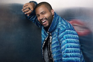 Projota sorrindo para fotos encostado com o braço na parede