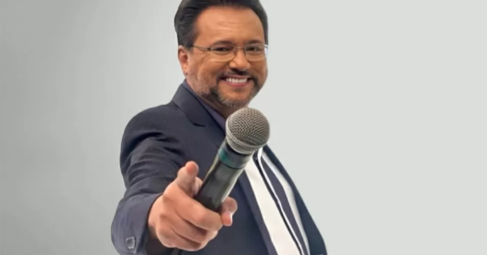 Geraldo Luís usando terno e segurando o microfone na frente da foto