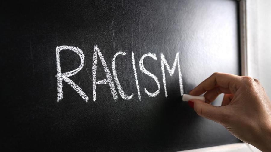 Pessoa escrevendo a palavra racismo em um quadro negro - Getty Images/iStockphoto